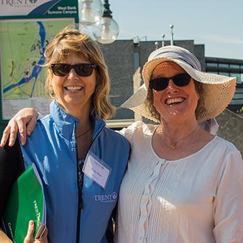 2 women in sunglasses, smiling at the camera, standing side by side outside of the Bata library on a sunny afternoon