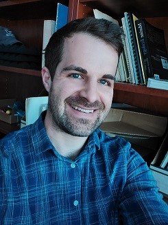Graham Raby smiling at the camera in front of a bookshelf.