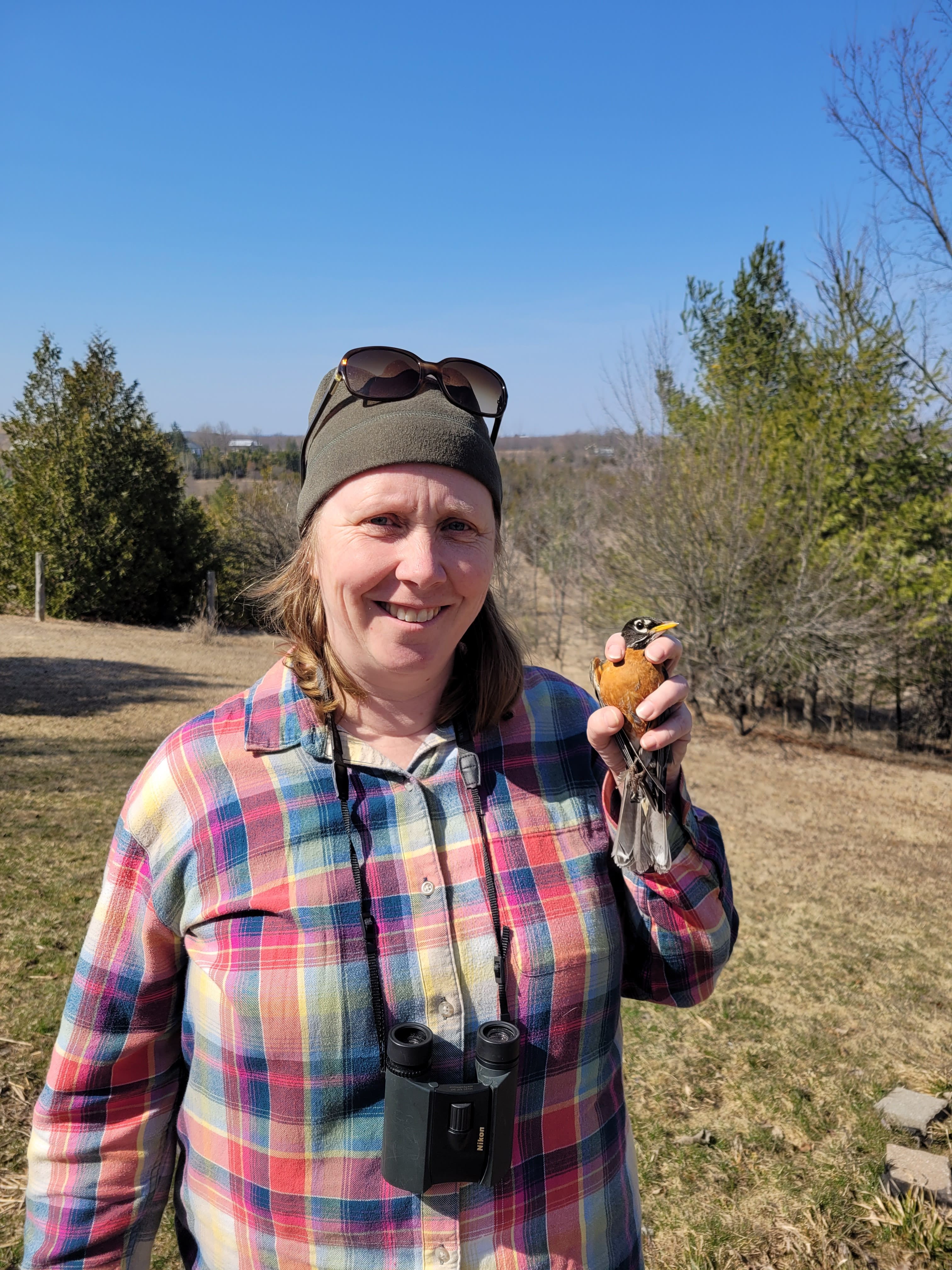 Sarah Jamieson smiling in a field while holding a Robin in her left hand.