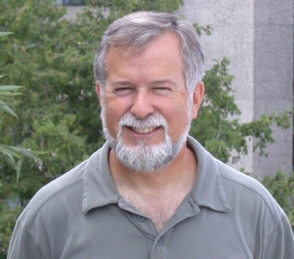 Michael Fox standing in front of trees and a Trent cement building wearing a grey shirt, smiling at the camera.
