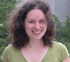 Maggie Xenopoulos standing in front of trees and a cement building on a windy day, wearing a green shirt and smiling at the camera.