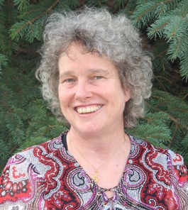 Smolly Coulson in front of a spruce tree wearing a red and grey paisley shirt, smiling at the camera.