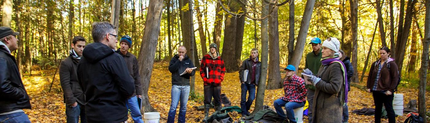 Dr. Michael Frost standing outside in the woods in the fall addressing a a group of students